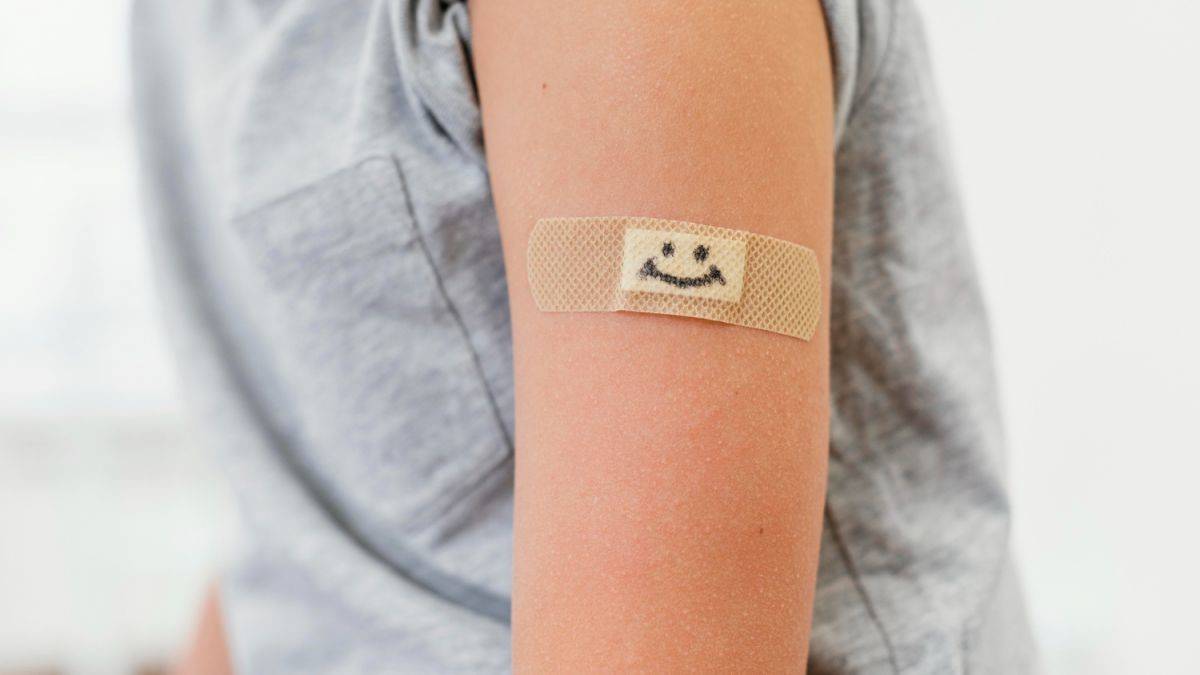 Пластир із намальованою усмішкою наклеєний на руку дитини у сірій футболці.
