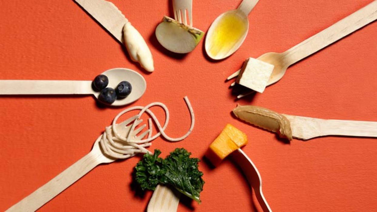 Набір дерев’яних столових приборів з різними продуктами — ягодами, овочами, пастою та соусами на помаранчевому фоні