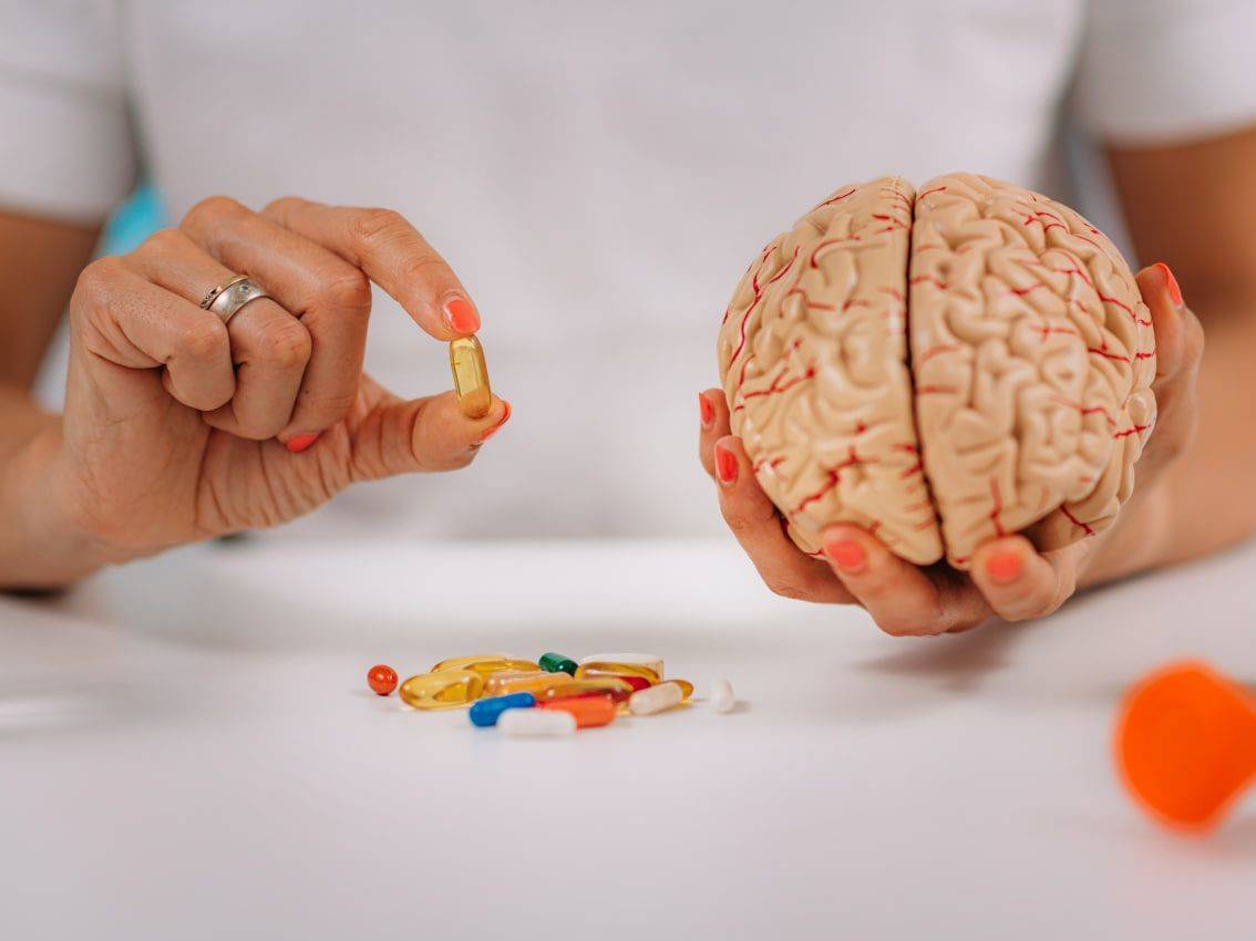 Рука лікаря тримає модель людського мозку та капсулу добавки для підтримки когнітивної функції.