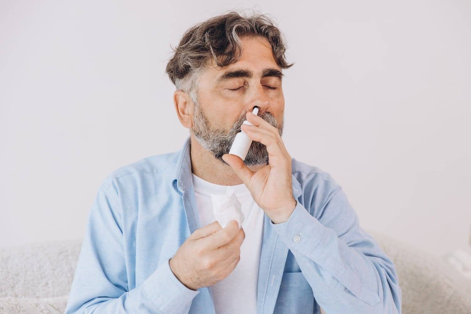 Чоловік використовує назальний спрей при нежиті та закладеності носа, симптоми риніту у дорослого